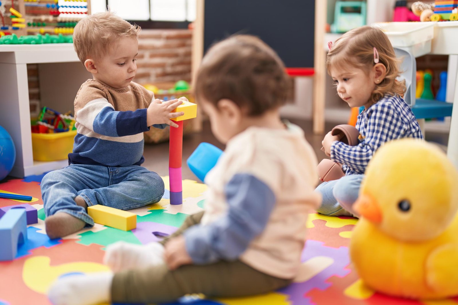 Toddlers engaged in playtime on a colorful mat, stacking blocks and exploring toys, fostering creativity and social interaction.