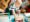 A curious toddler joyfully explores a wooden drum, tapping with a mallet while surrounded by musical instruments and toys in a playful learning environment.