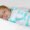 A peaceful newborn baby sleeps soundly, swaddled in a cozy white blanket adorned with pastel-colored whale patterns in shades of blue, pink, and gray. The baby's delicate hand rests gently on the soft fabric, and their serene expression reflects comfort and warmth.