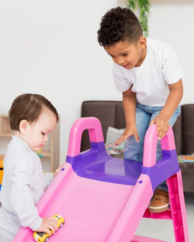 Two toddler boys playing with a pink and purple slide. One boy is climbing the slide getting ready to go down and the other boy is moving a yellow car up the slide