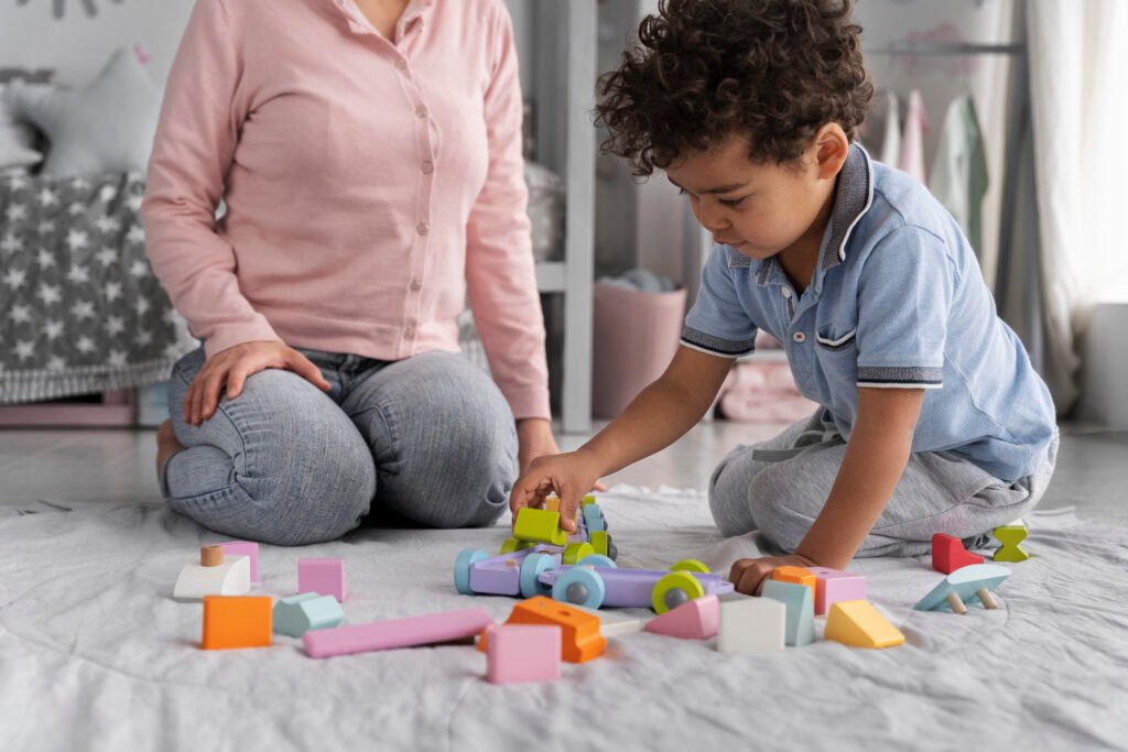 Little boy sitting on the floor with his mom, building a train out of colorful blocks.