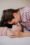 A mother and her baby lying on a bed, gazing lovingly into each other's eyes. The mother leans in close, touching her forehead to her baby's, both dressed in matching pink-striped outfits. The moment captures warmth and affection in a cozy setting.