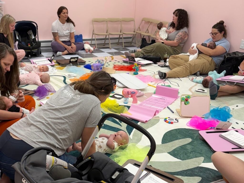 A provider leads a Mom Village session as moms hold and care for their newborns on a play mat at Baby University