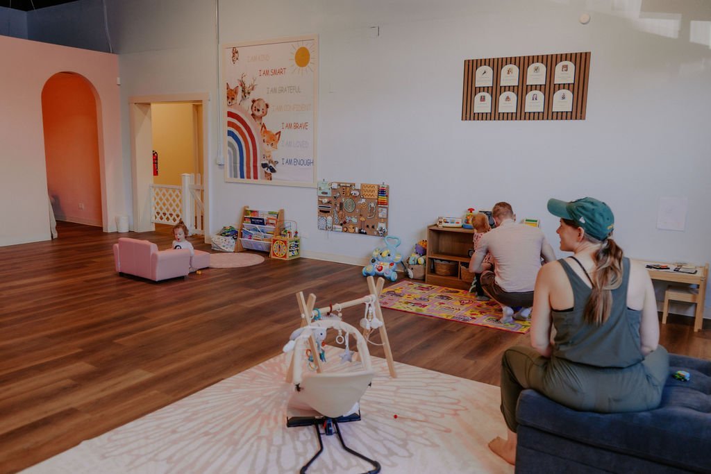 A mom relaxing on the couch while kids play in the gated parents lounge at Baby University
